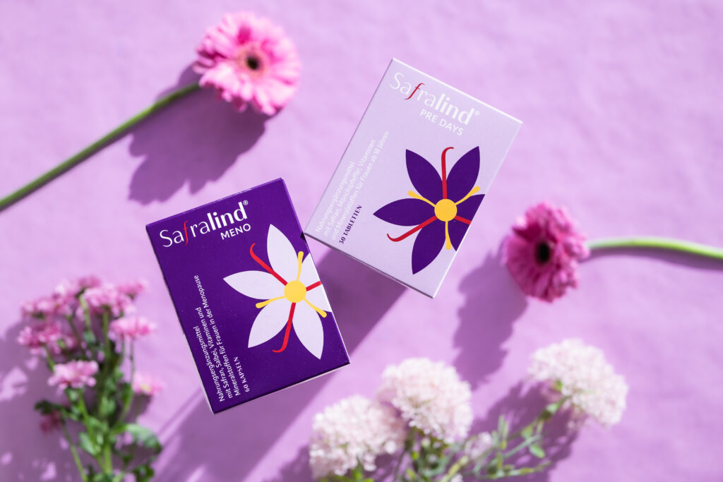 Safralind Meno und Pre Days Produkte auf violettem Hintergrund mit Blumen für Wechseljahre und PMS.